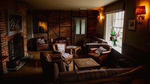 A cozy living room with brick walls, leather furniture, and a fireplace. - The Hawk Inn (Andover)
