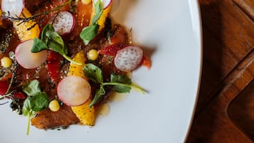 A white plate with a dish of food, including slices of radish, herbs, and possibly some citrus.