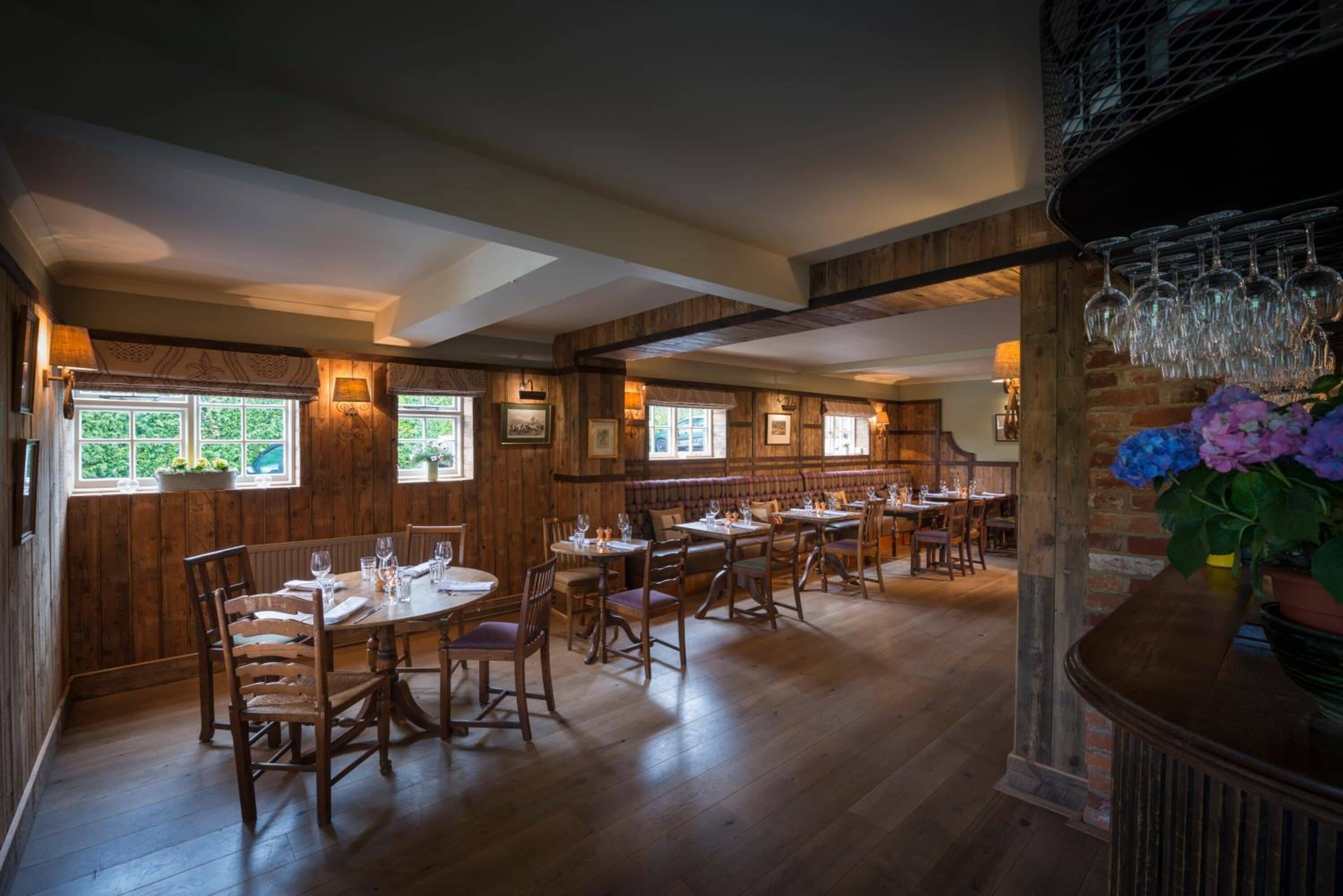 A restaurant with wooden walls and large windows, multiple tables and chairs, and a chandelier.