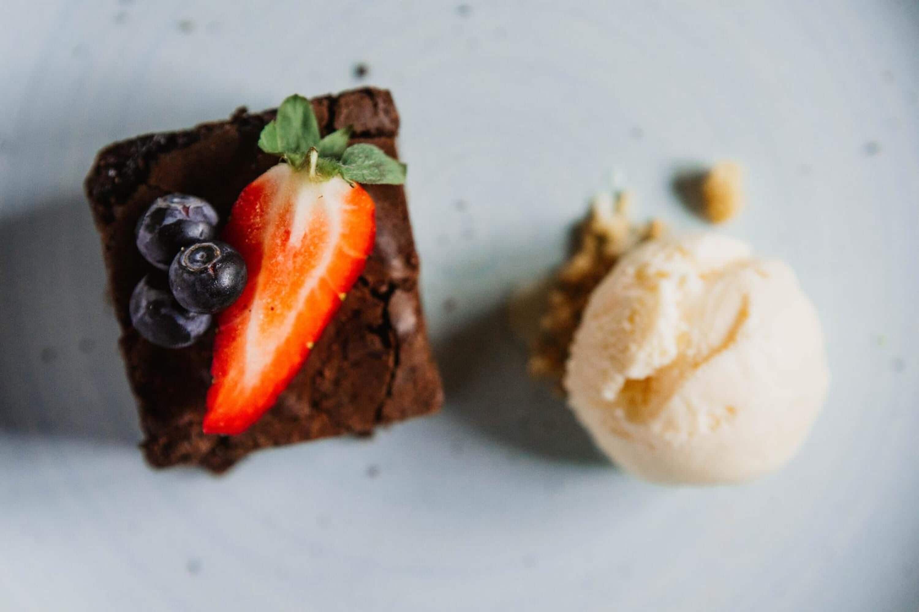 A dessert with a brownie topped with a strawberry and blueberries, and a scoop of vanilla ice cream.