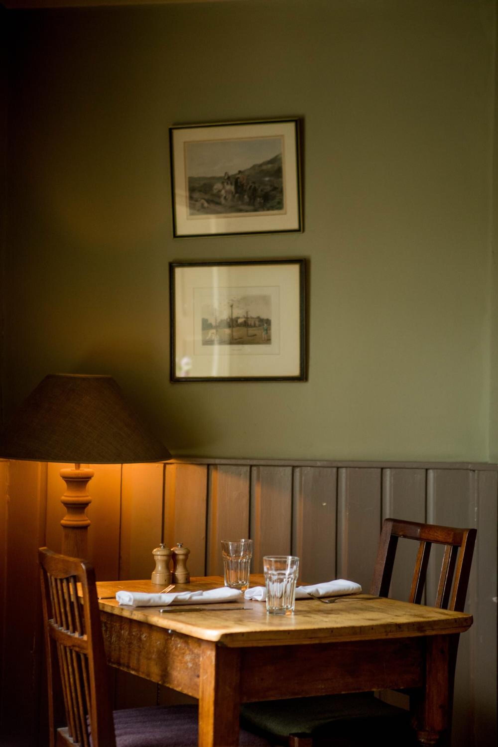 A dining table with chairs, a lamp, salt and pepper shakers, and two framed pictures on the wall.
