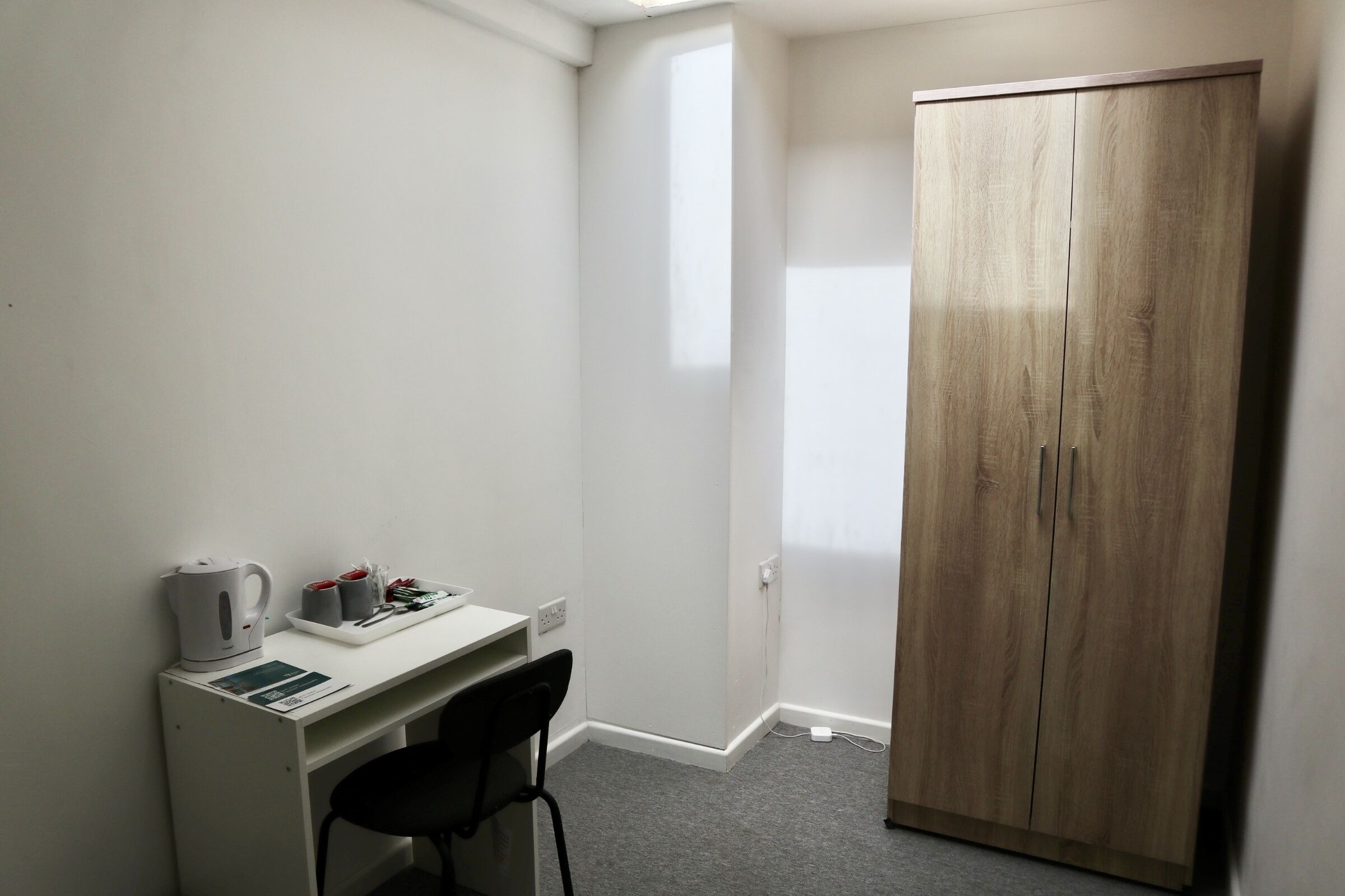 Quarto pequeno com escrivaninha, cadeira e guarda-roupa.