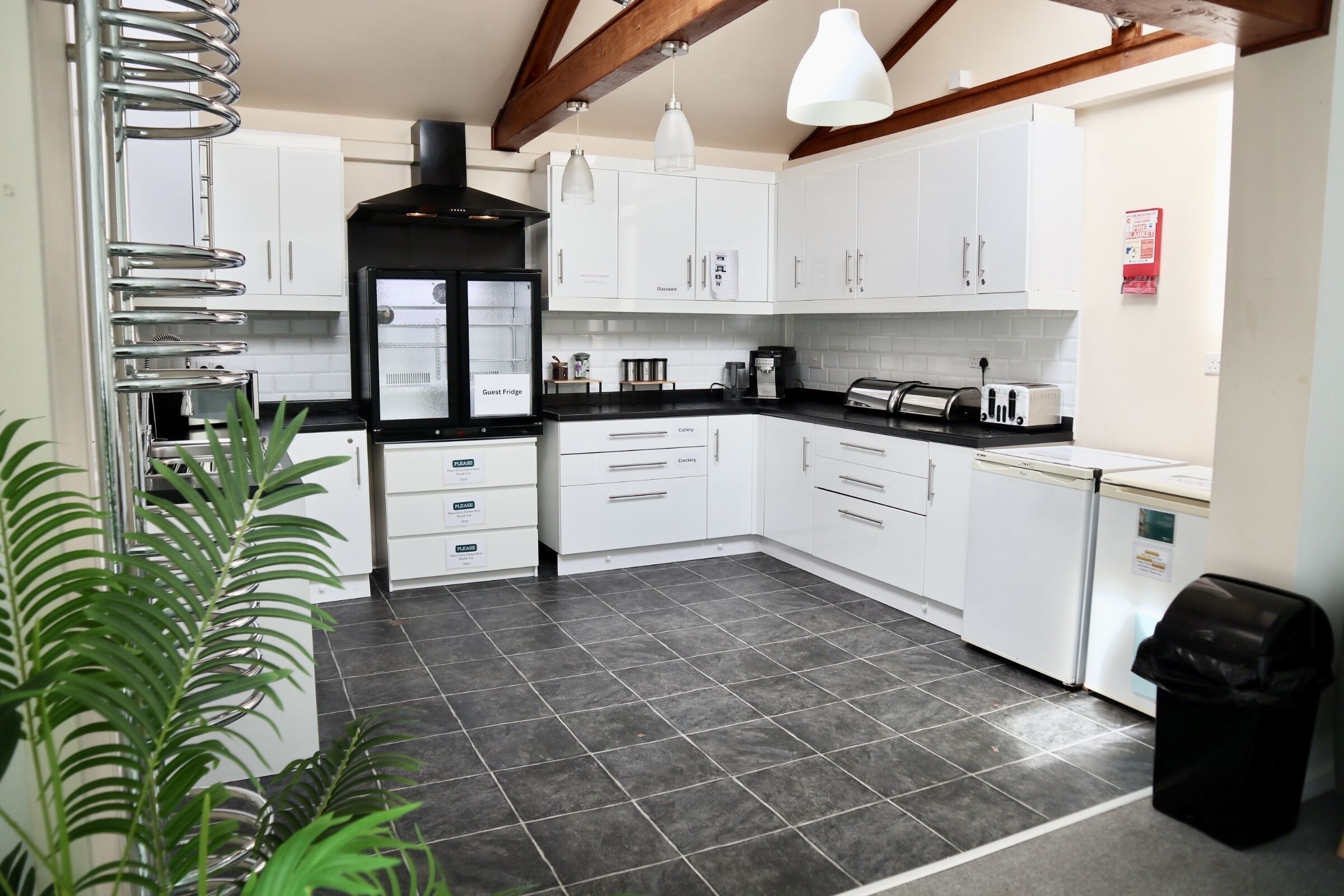 A modern kitchen with white cabinets, a black countertop, and a black trash bin.