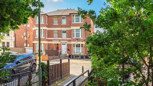 A multi-story brick building with a red door, a visible sign, and a parking area with a blue car. - City Centre Guest House - Gloucester Park (Gloucester)