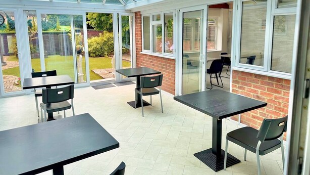 A conservatory with glass walls, a brick wall, and a patio area with tables and chairs. - City Centre Guest House - Gloucester Park (Gloucester)