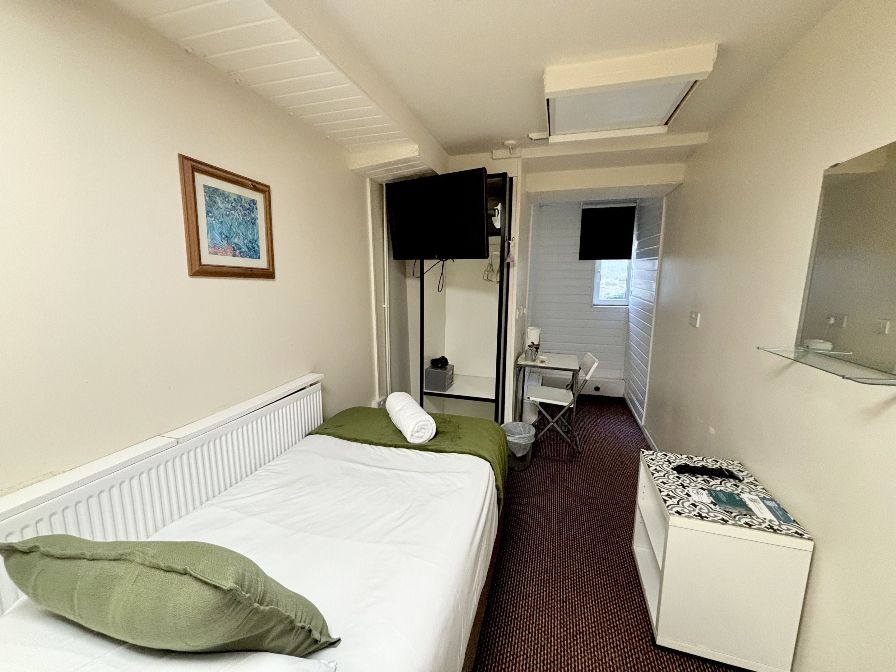 Una habitación de hotel con una cama, un escritorio, una silla, un televisor y una ventana pequeña.