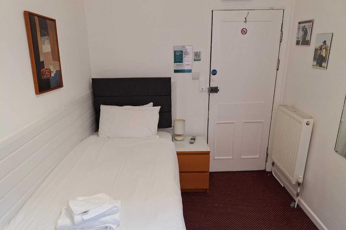 A hotel room with a bed, a nightstand, a door, and a radiator.