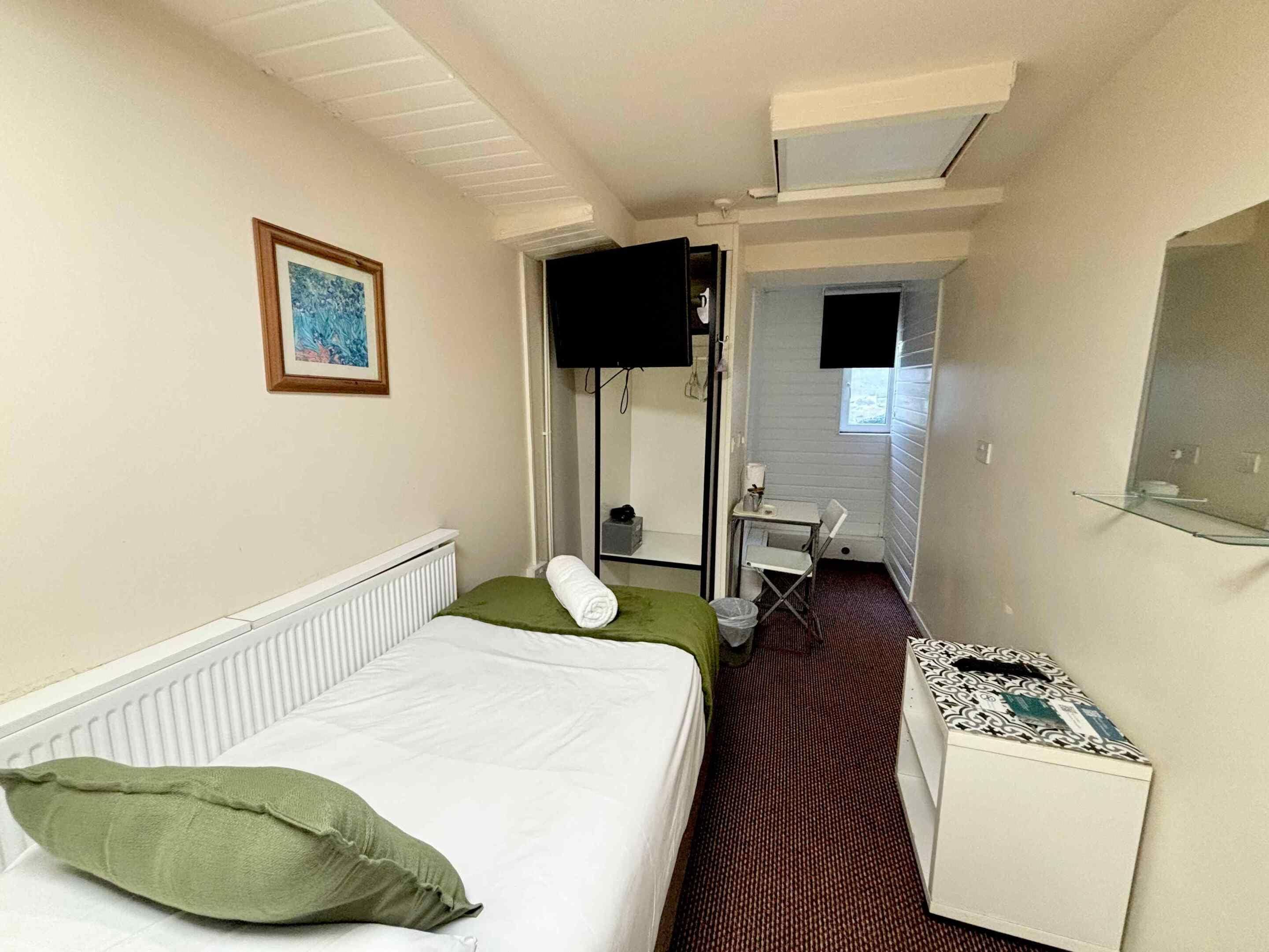 A hotel room with a bed, a desk, a chair, a television, and a window.