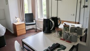 Una habitación de hotel con una cama, un escritorio con una bandeja de tazas, una tetera y un control remoto.