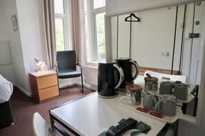 Una habitación de hotel con una cama, un escritorio con una bandeja de tazas, una tetera y un control remoto.