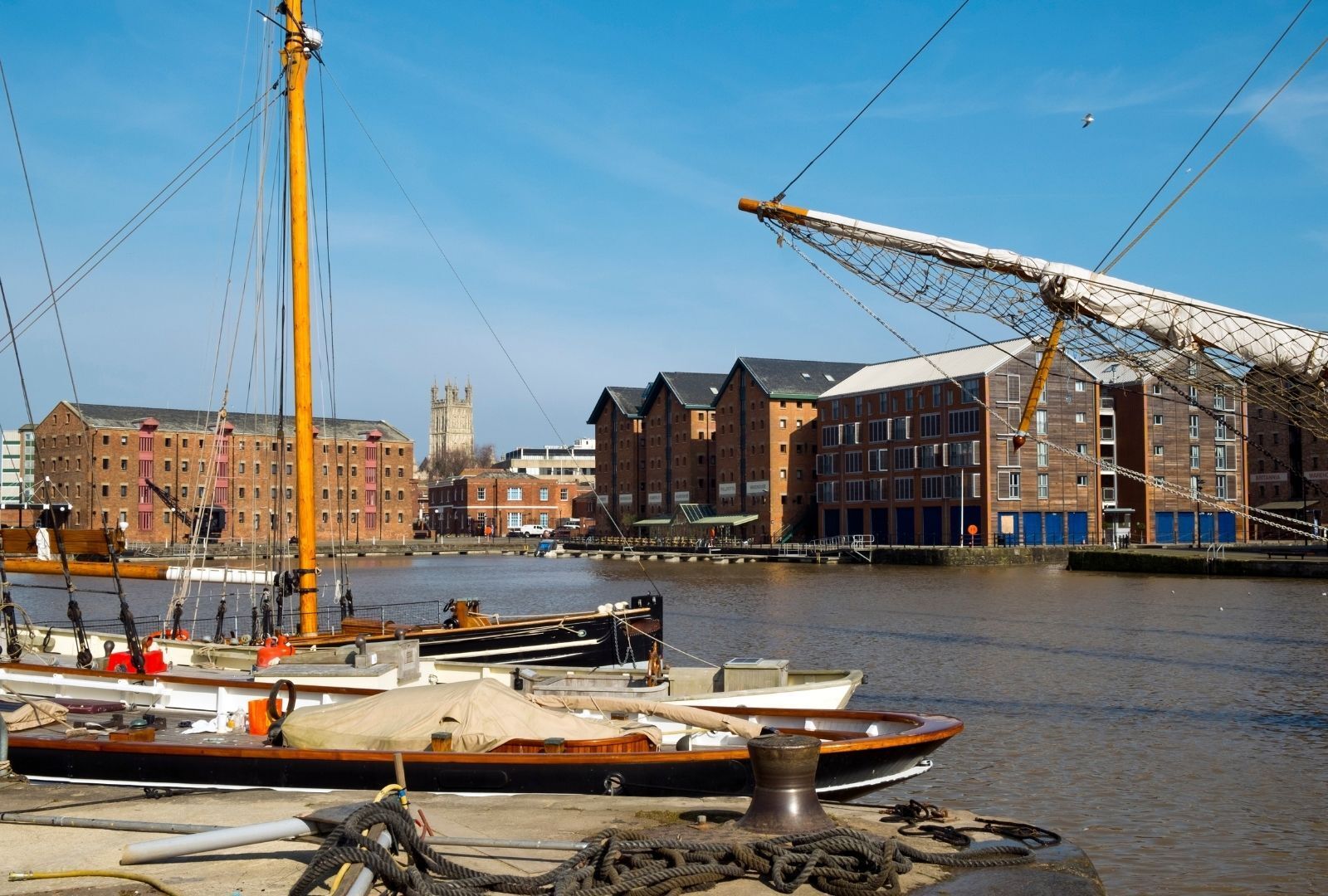 A harbor with boats docked, a crane, and buildings in the background.