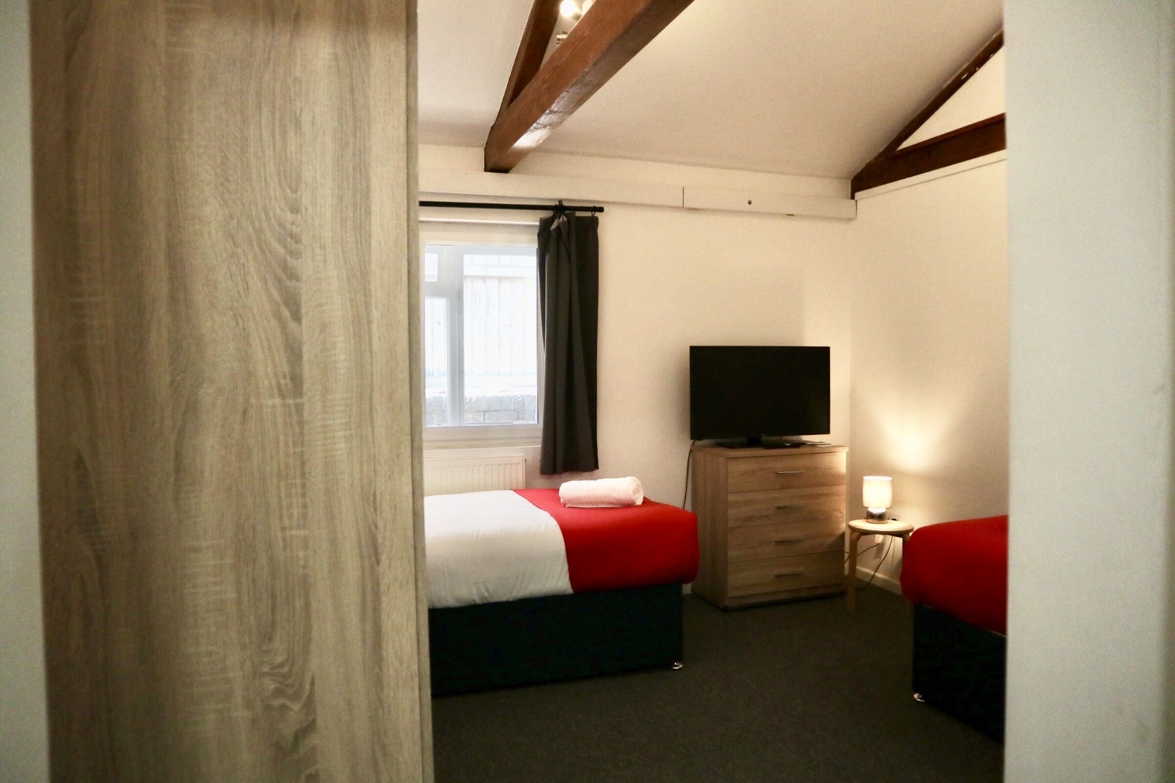 Une chambre avec deux lits, une télévision, une commode et une fenêtre avec des rideaux.