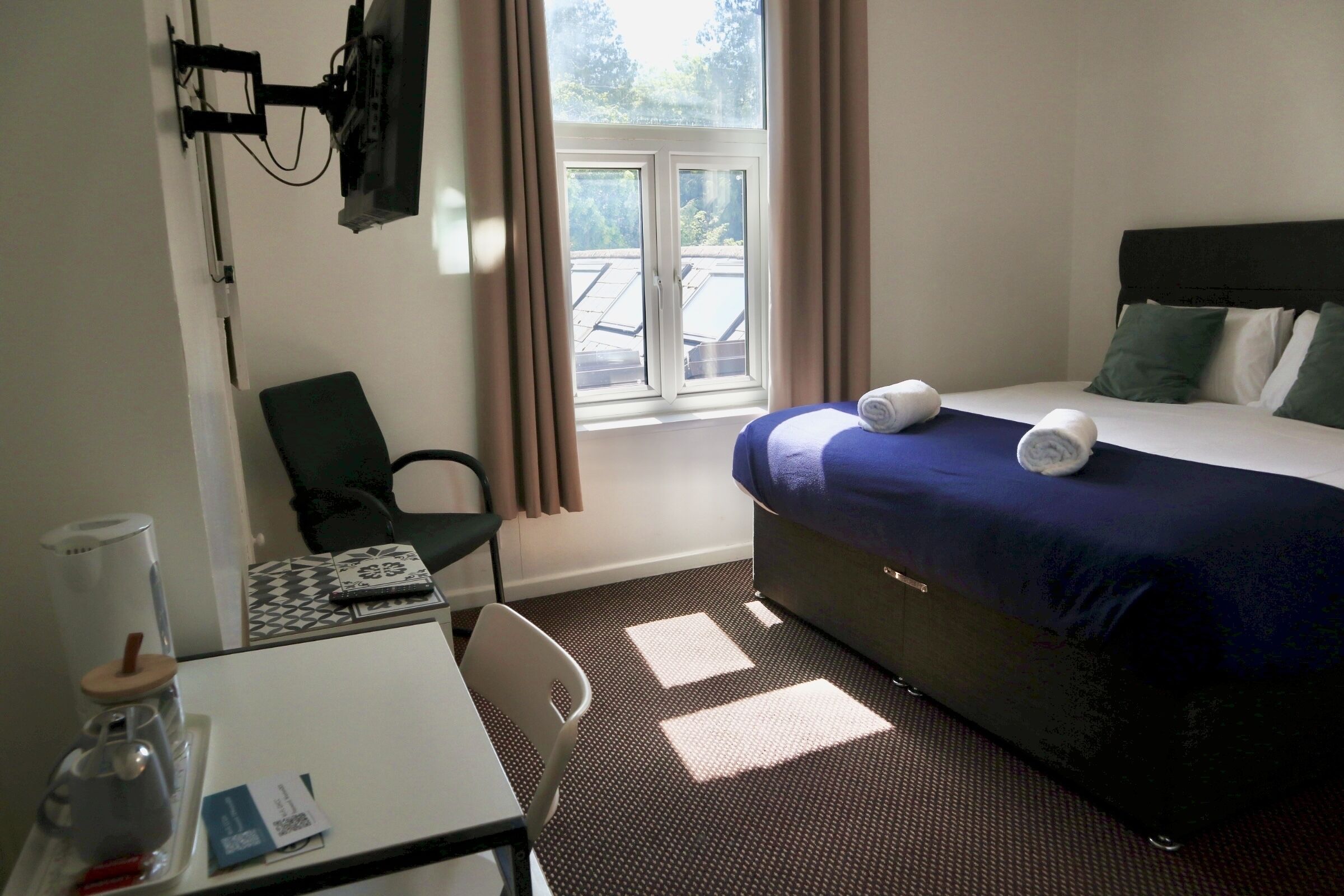Habitación de hotel con cama, escritorio, silla, televisión montada en la pared y ventana con cortinas.