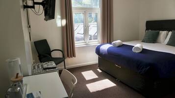 Habitación de hotel con cama, escritorio, silla, televisión montada en la pared y ventana con cortinas.