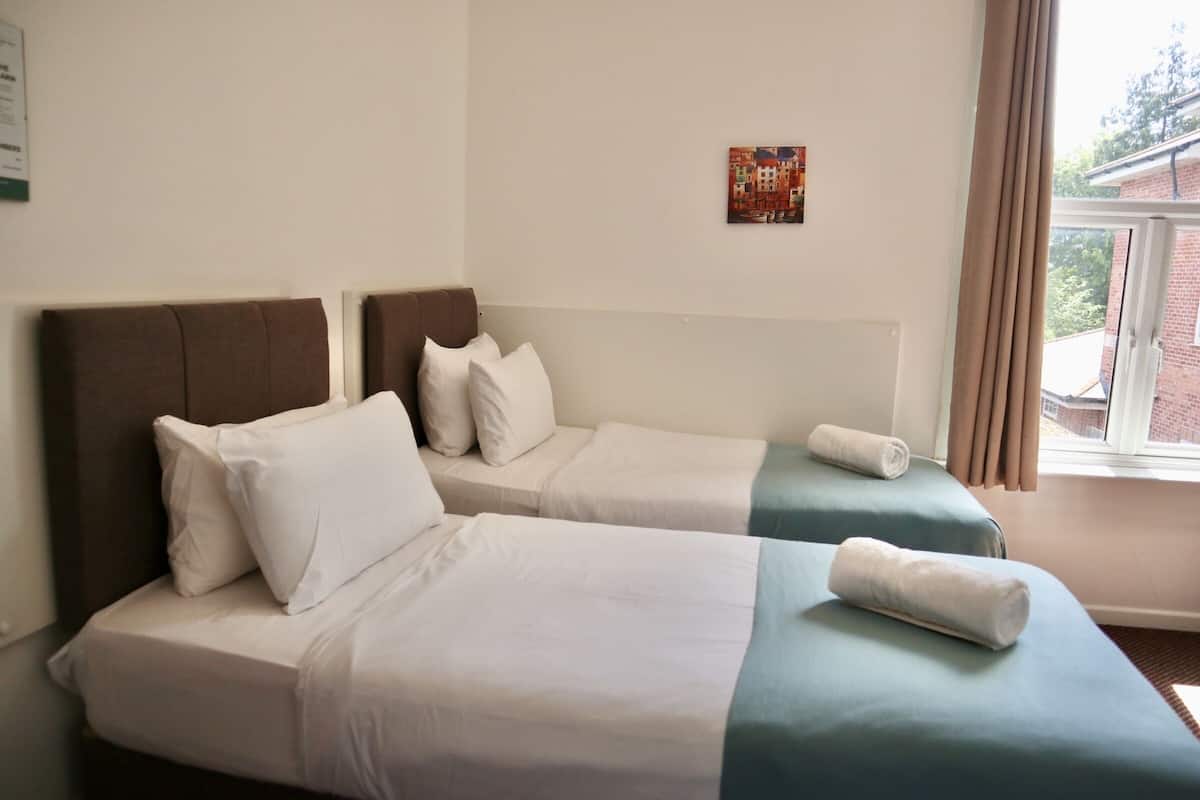 A hotel room with two beds, a window with curtains, a wall-mounted artwork, and a view of the outside.