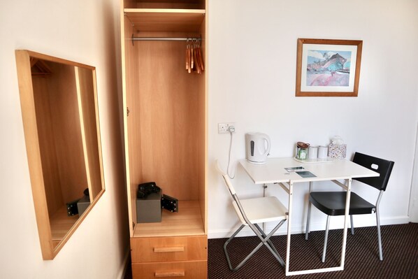 Habitación funcional con un armario de madera, un escritorio blanco con silla, un cuadro en la pared y una cafetera.