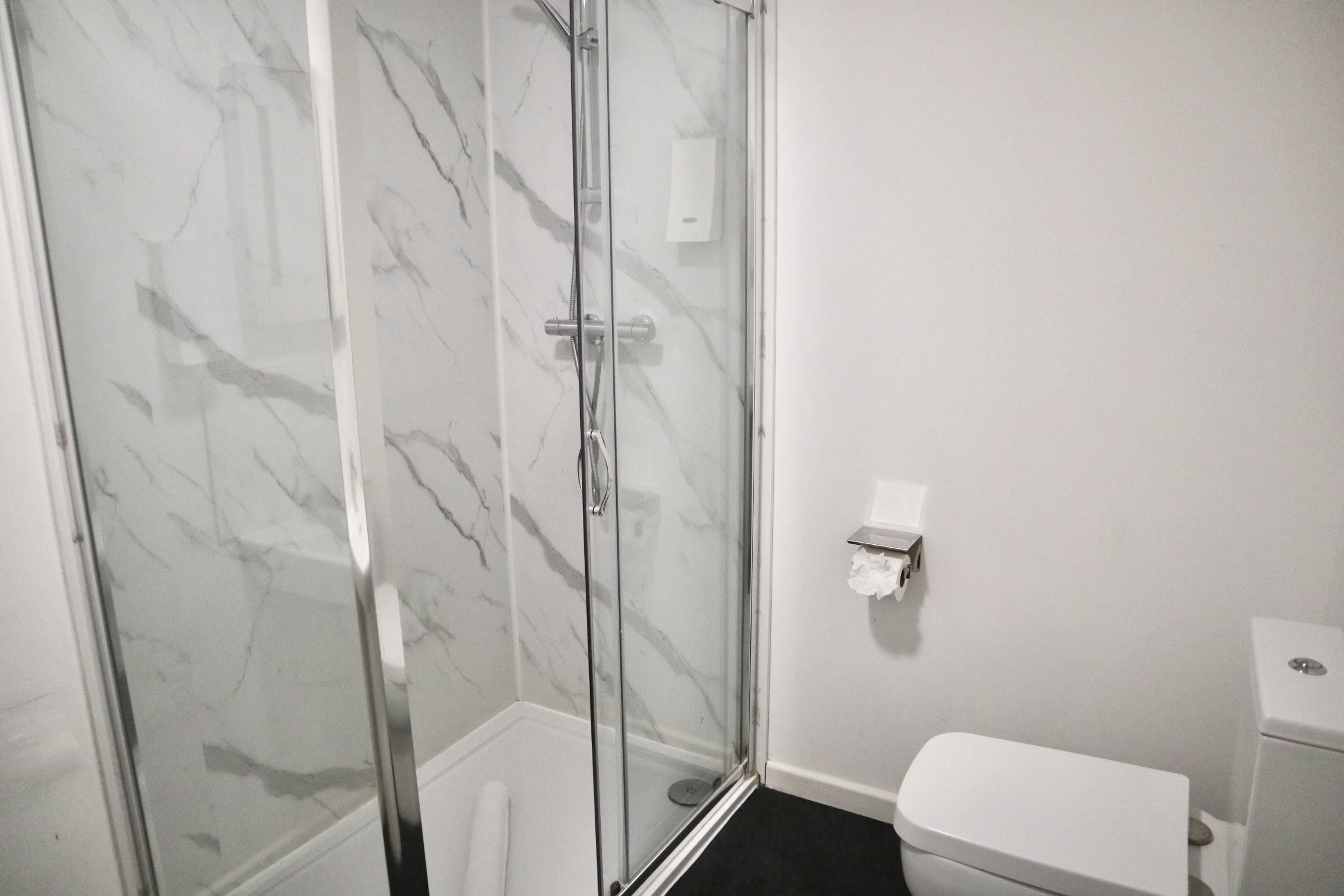 A bathroom with a glass-enclosed shower, a toilet, and a marble-patterned wall.