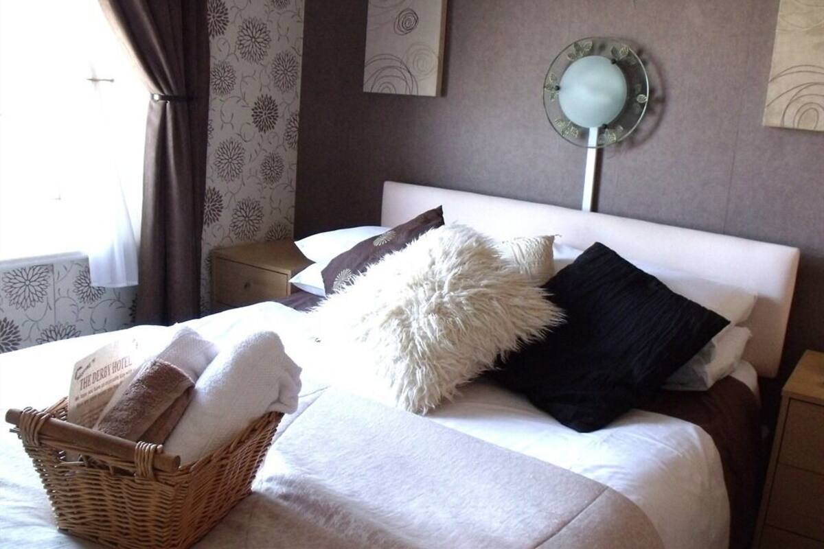 A neatly made bed with a basket of towels, a fluffy pillow, and a dark pillow.