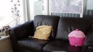A black leather sofa with a beige and a pink pillow, a small round ottoman, and a decorative vase with flowers. - The Derby Hotel (Blackpool)