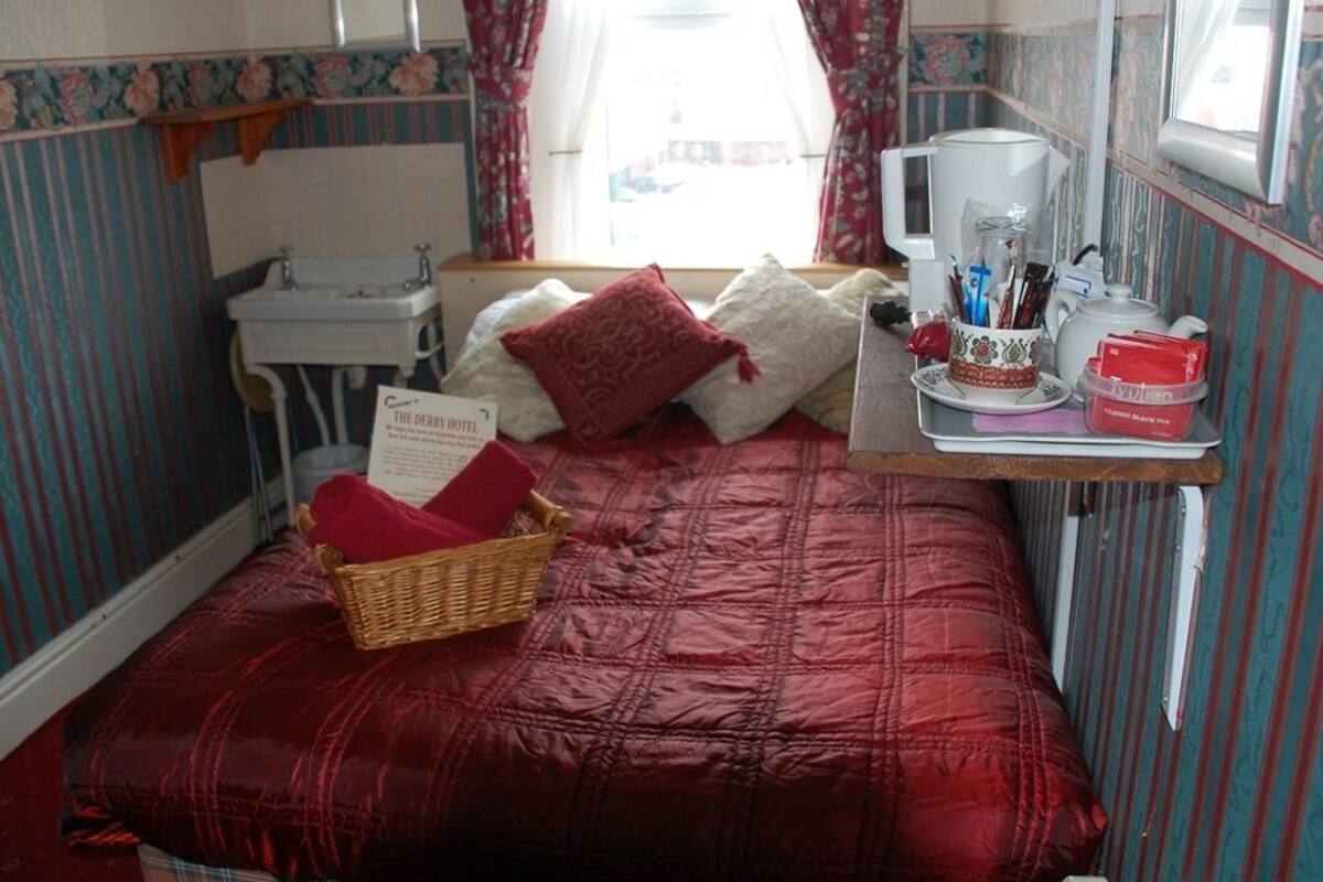 A bedroom with a red quilted bedspread, a wooden nightstand with a basket, a white sink, and a window with curtains.