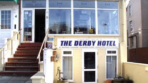 The exterior of The Derby Hotel with a signboard, a staircase leading to the entrance, and a small outdoor seating area with potted plants. - The Derby Hotel (Blackpool)