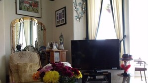 A living room with a television, a floral arrangement, a chair, and a table with items on it. - The Derby Hotel (Blackpool)