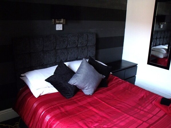 A bed with a red blanket, black and gray pillows, and a dark headboard. - The Derby Hotel (Blackpool)