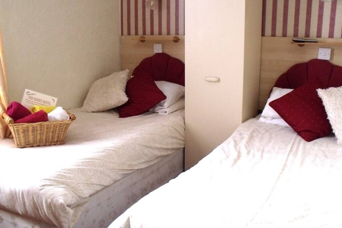 Two single beds with red pillows, a wicker basket with towels, and a sign for The Derby Hotel.
