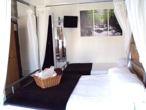 A bedroom with two beds, a mirror, a television, and a painting of a forest scene. - The Derby Hotel (Blackpool)