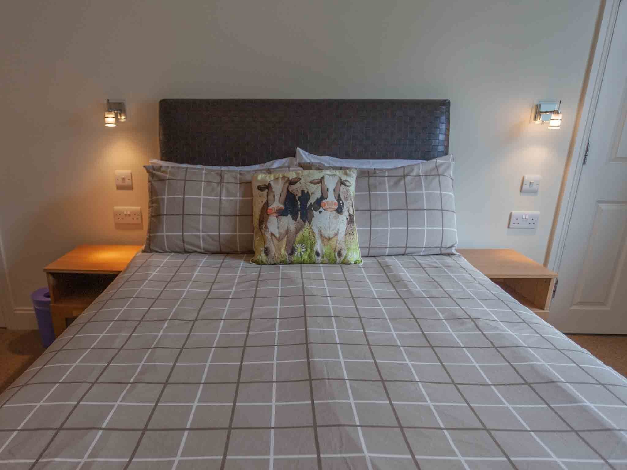 Una cama con cabecera, dos mesitas de noche y una lámpara fijada a la pared.