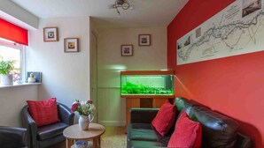 Un salon avec un mur d’accent rouge, un aquarium, deux canapés en cuir avec des coussins rouges et une petite table sur laquelle est posé un vase de fleurs.