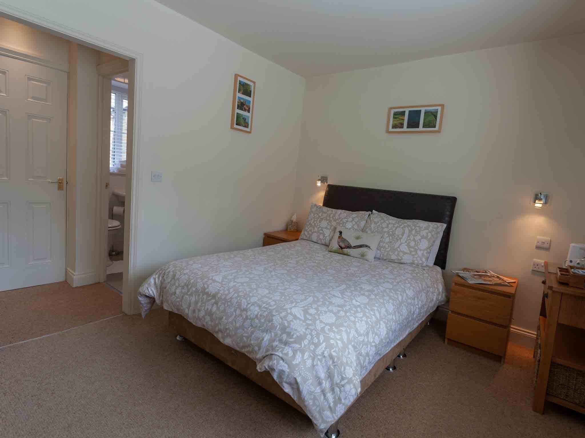A bedroom with a bed, two bedside tables, a nightstand, and a door leading to a bathroom.