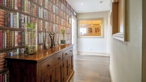 A hallway with a wooden floor, a bookshelf filled with books, and a cabinet with drawers. - The Highworth Hotel (Swindon)
