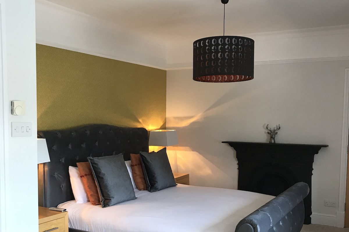 A bedroom with a bed, a nightstand, a lamp, a fireplace, and a wall with a textured pattern.