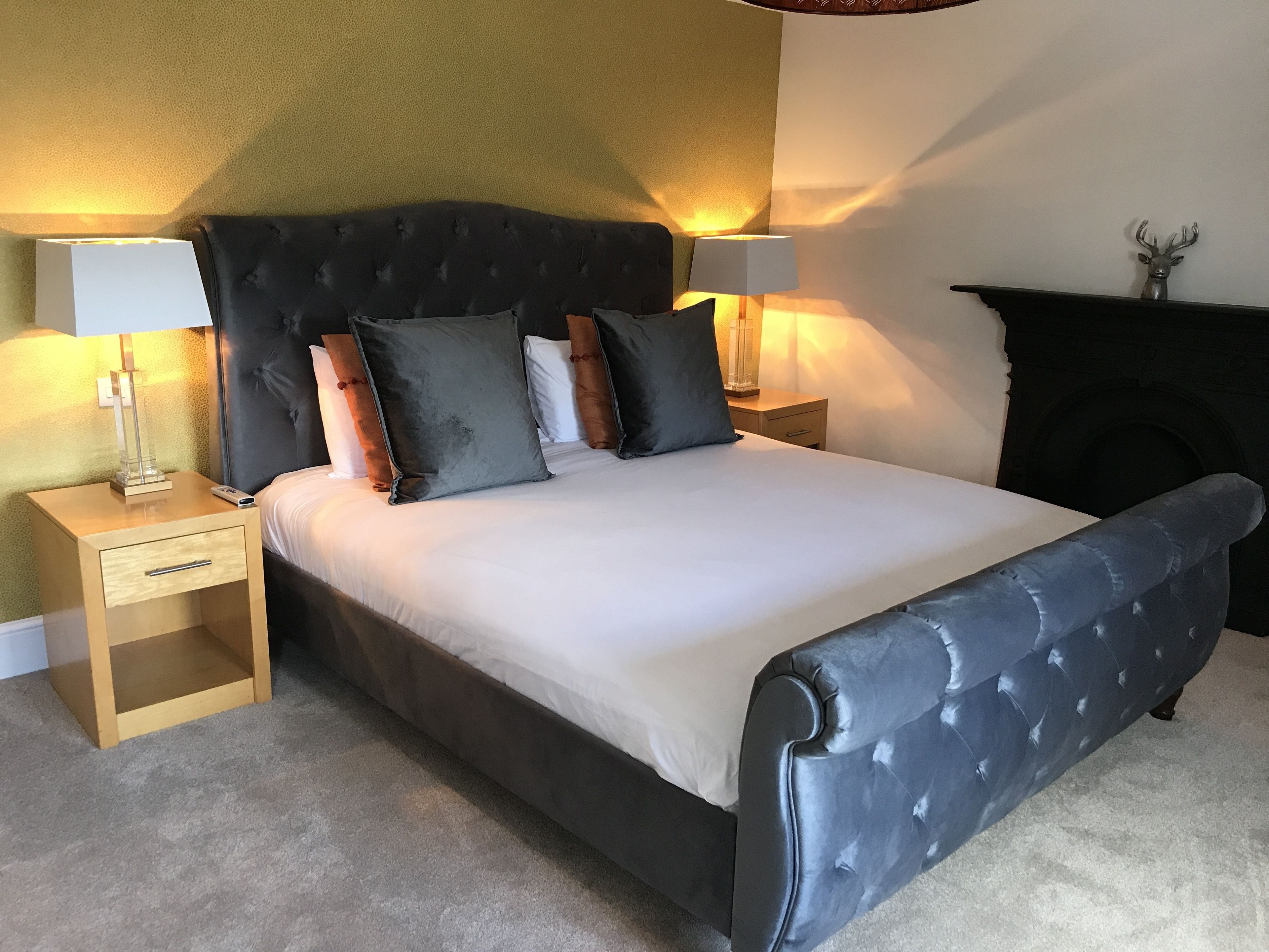 A bedroom with a large bed, two bedside tables, a nightstand, a lamp, and a fireplace.
