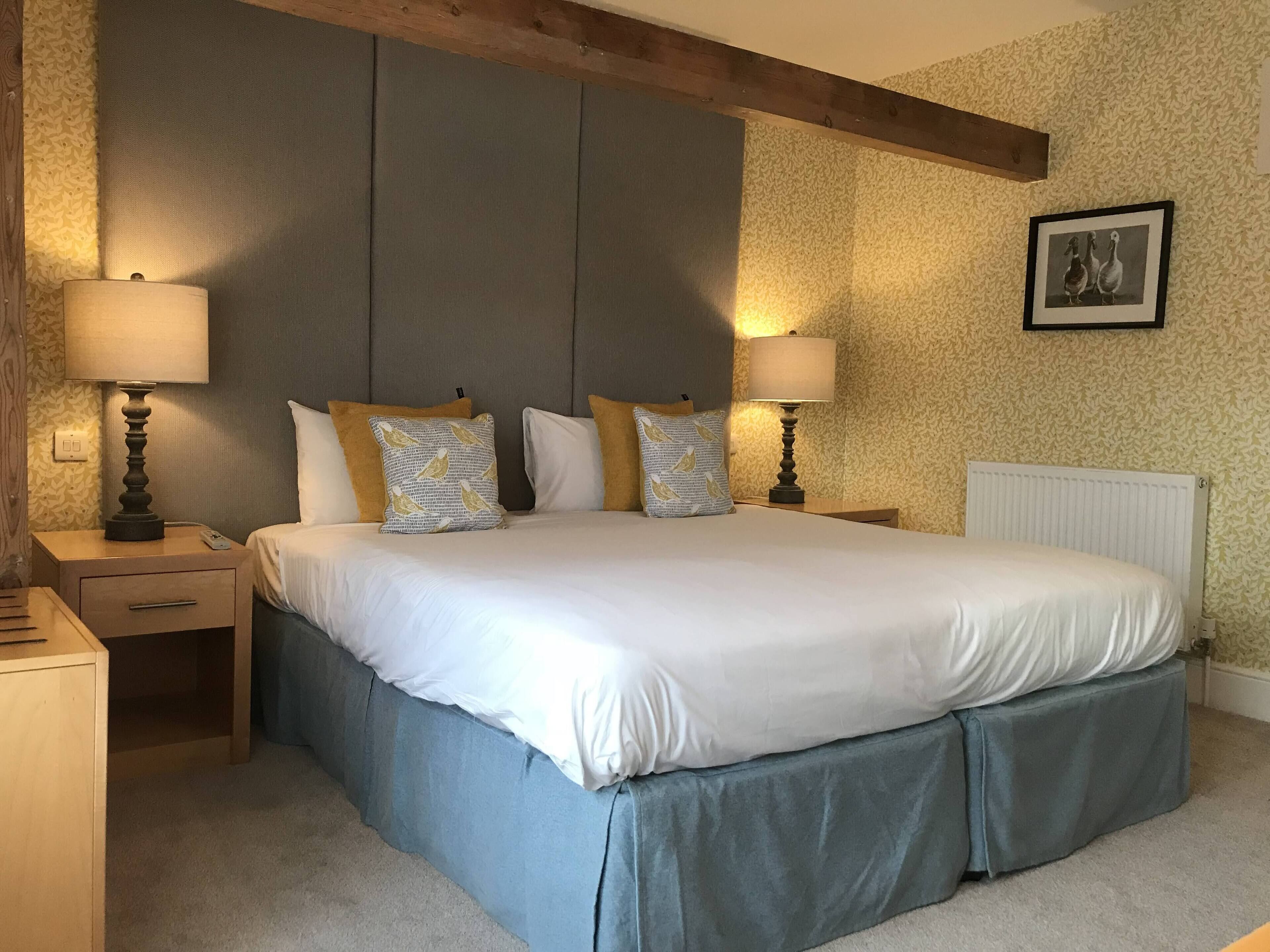 A neatly made bed with a grey headboard, two bedside tables with lamps, and a framed picture on the wall.