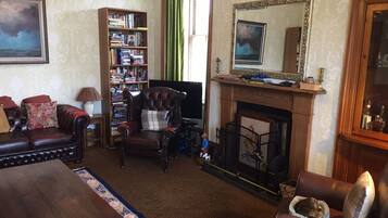 A cozy living room with a fireplace, leather armchairs, a bookshelf, and a television.