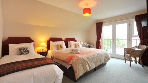 A hotel room with two beds, a balcony, a TV, and a chair. - Dunallan House (Grantown-on-Spey)