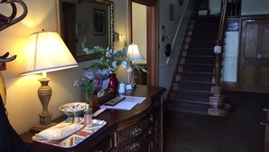 A hotel lobby with a wooden staircase, a desk with a lamp, a vase with flowers, and a mirror on the wall. - Dunallan House (Grantown-on-Spey)