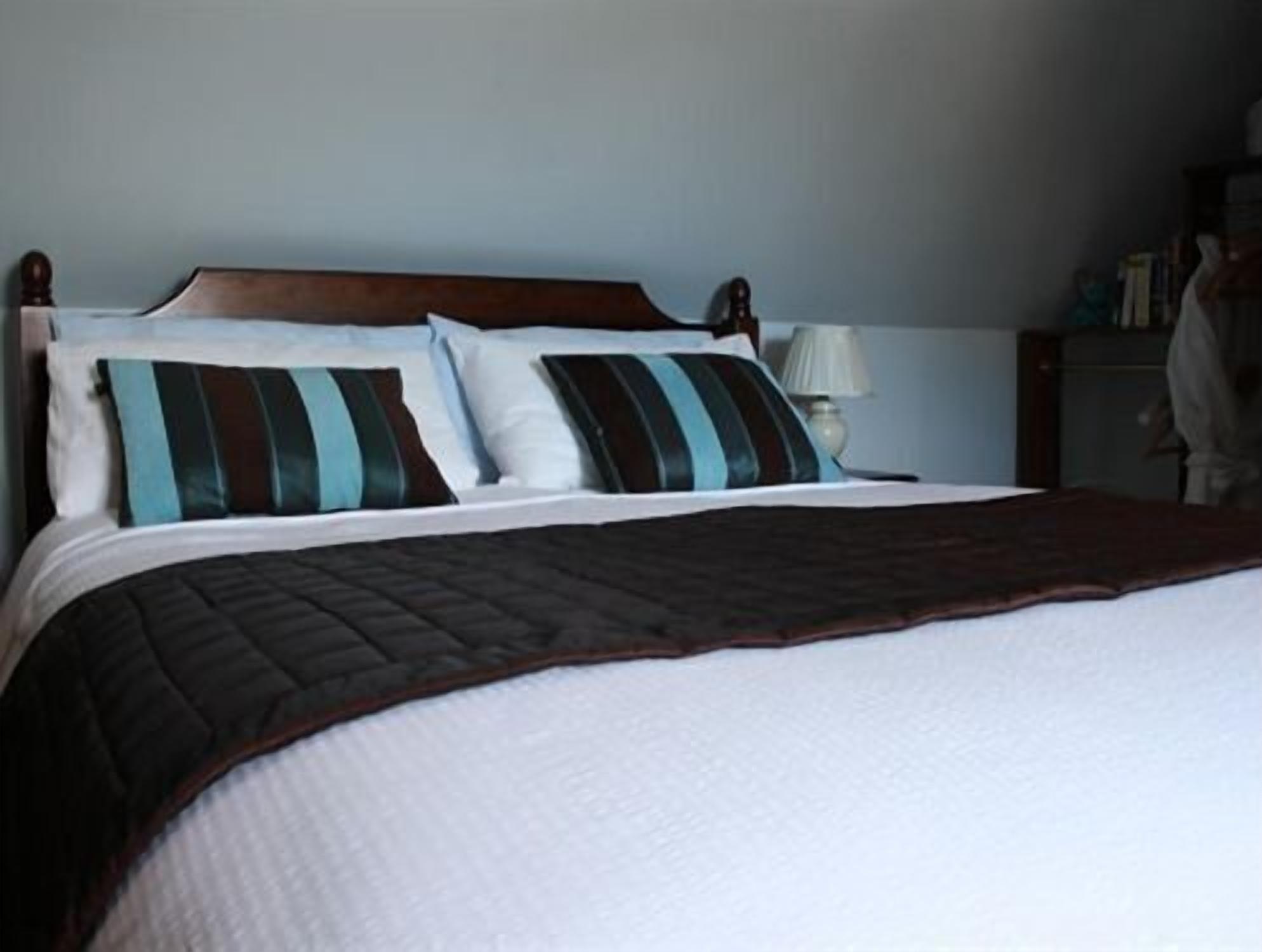 A neatly made bed with striped pillows and a dark brown blanket.