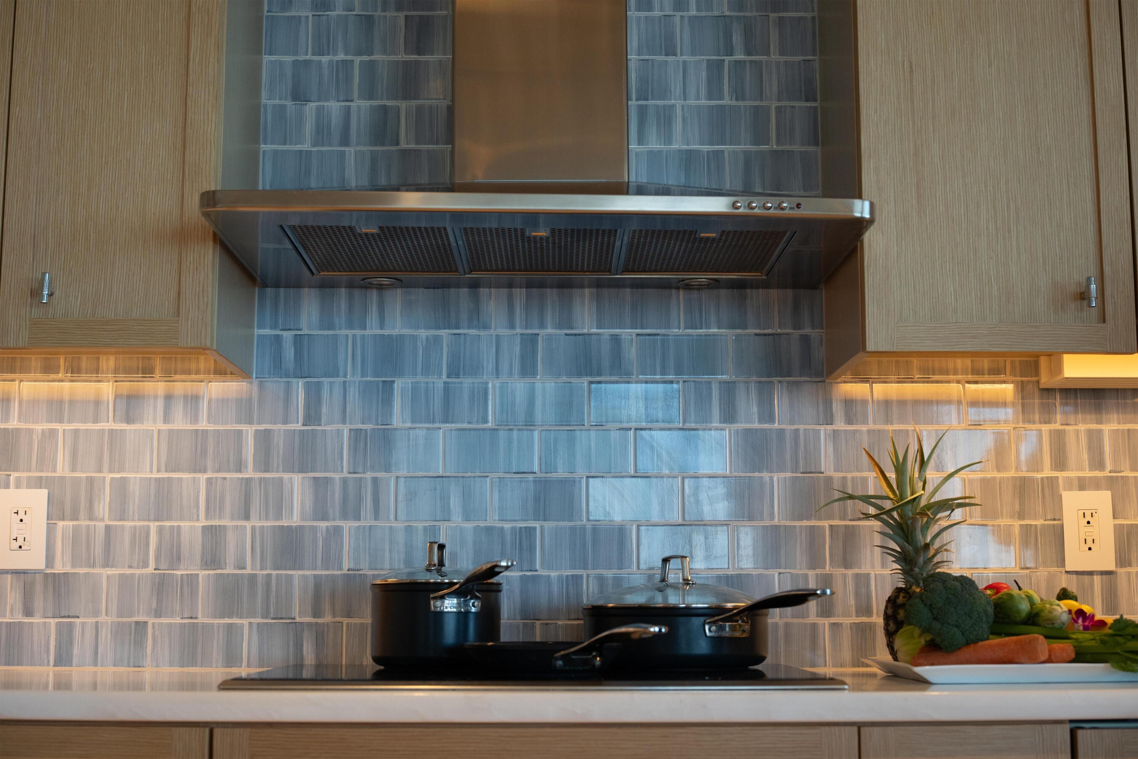 Una cocina con extractor de acero inoxidable, salpicadero de azulejos y una encimera con ollas.