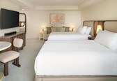 A hotel room with two beds, a TV, a desk with a chair, and a small table.
