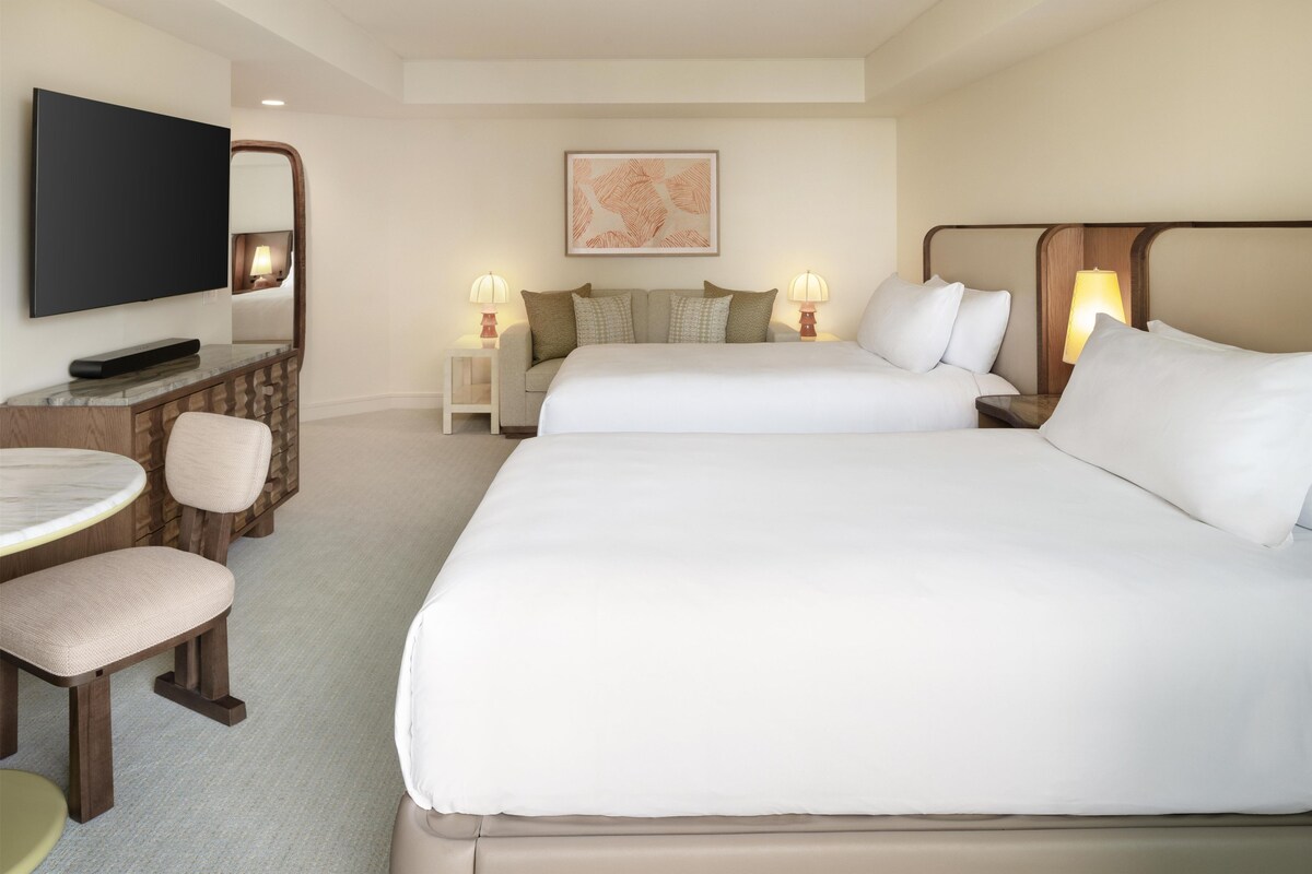 A hotel room with two beds, a TV, a desk with a chair, and a small table.