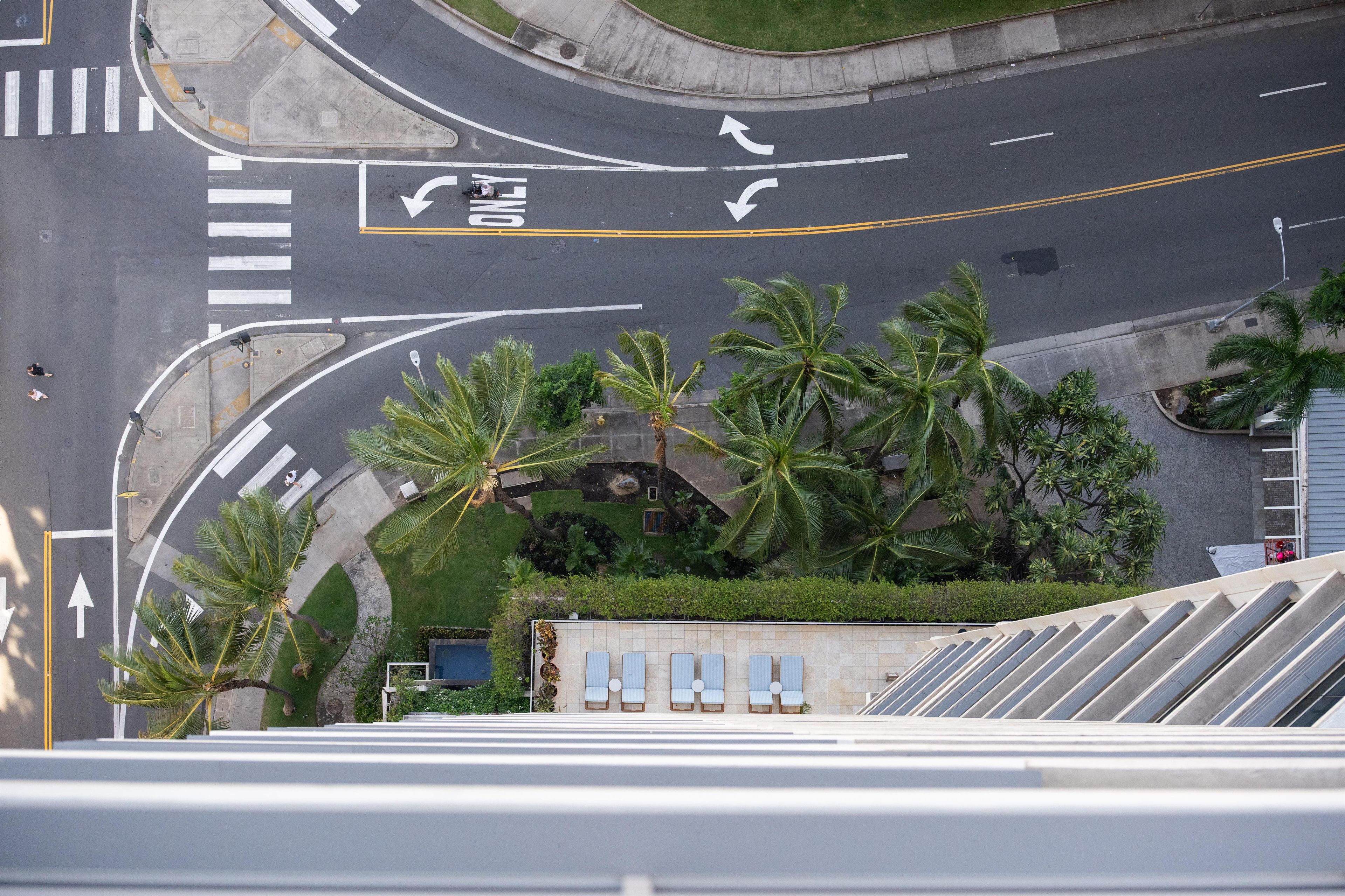 An aerial view of a road intersection with palm trees, a pool, and a building with a sloped roof.