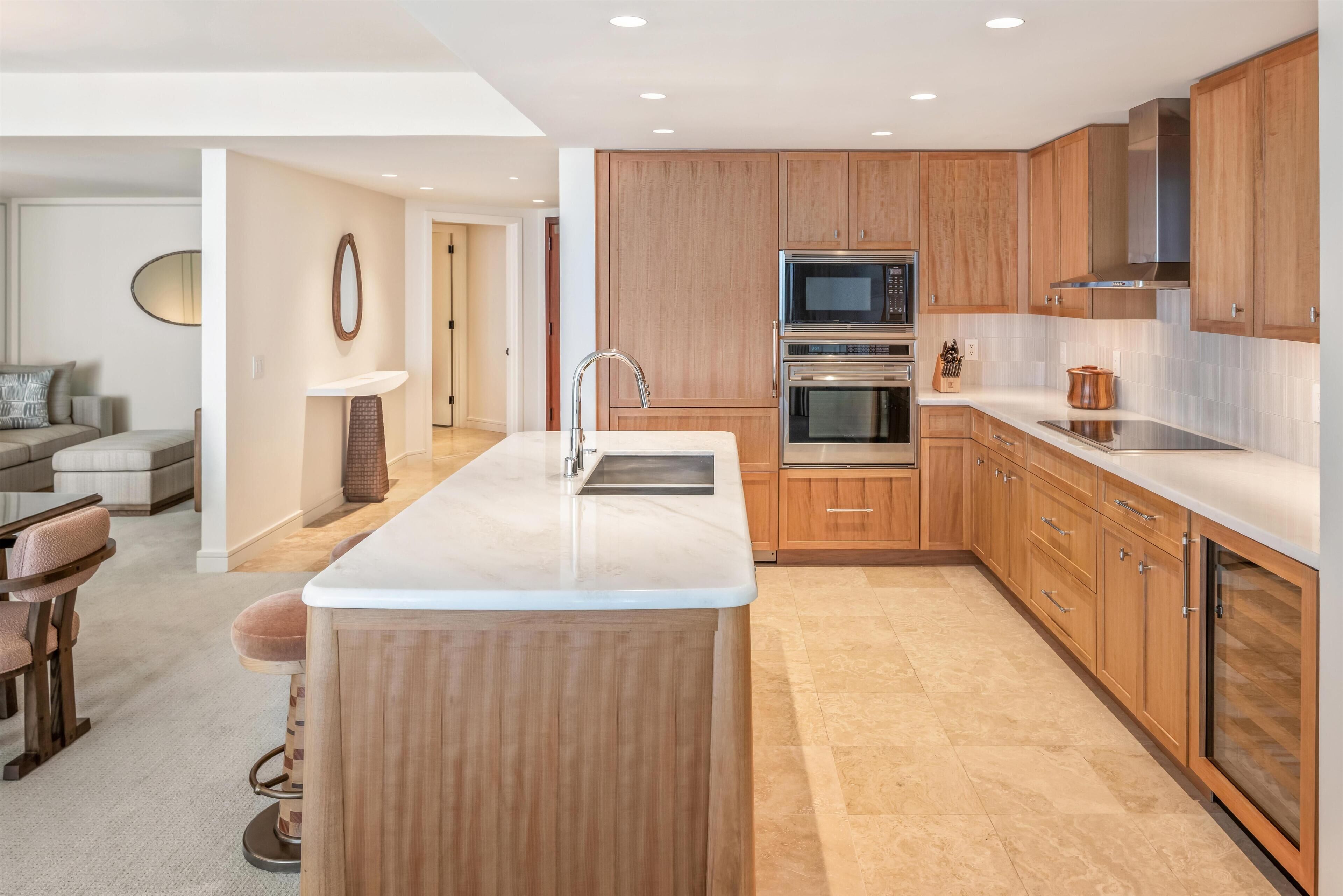 A modern kitchen with wooden cabinets, a central island, stainless steel appliances, and a bar stool.