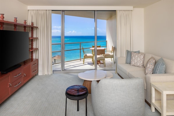 A hotel room with a balcony, a TV, a sofa, a small table, and a chair.