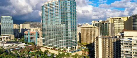 A high-rise hotel with a modern glass facade, surrounded by other buildings and palm trees.