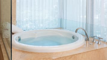 A large, oval-shaped hot tub in a modern bathroom with a glass partition and a view of tall buildings.