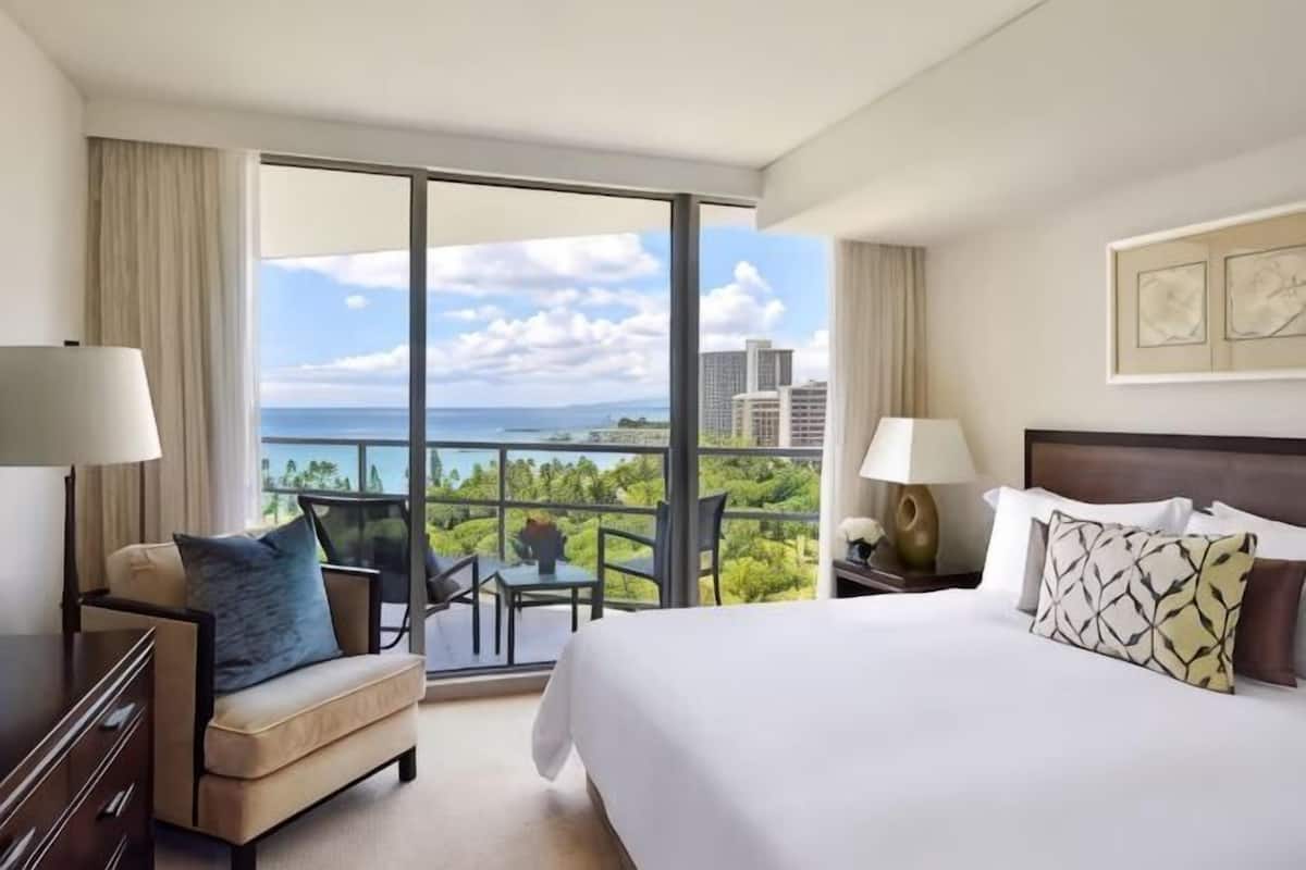 A hotel room with a large bed, a sofa, a table, and a view of the ocean.