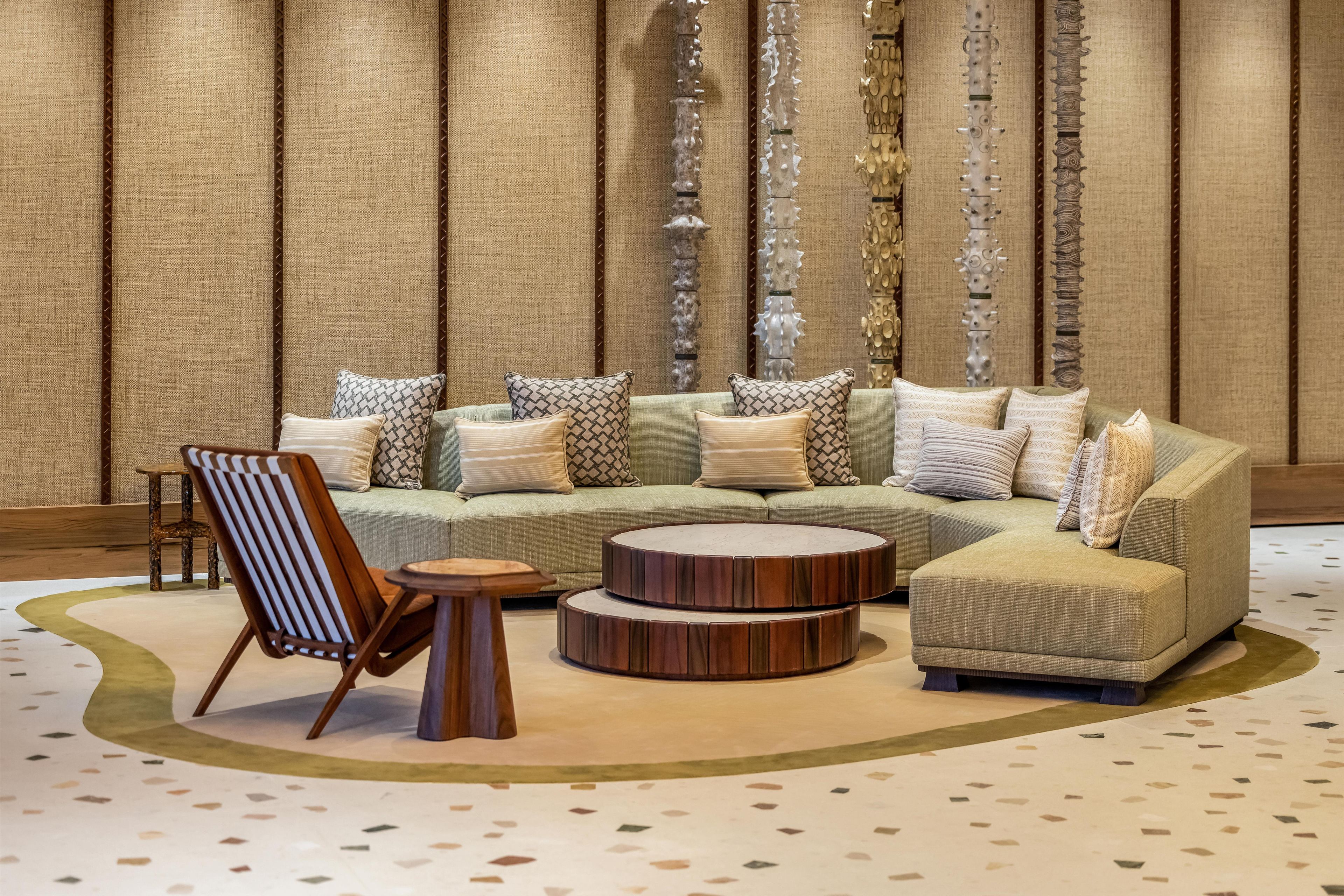 Un salon moderne avec un canapé d’angle, une table basse ronde, une chaise en bois et un tapis à motifs.